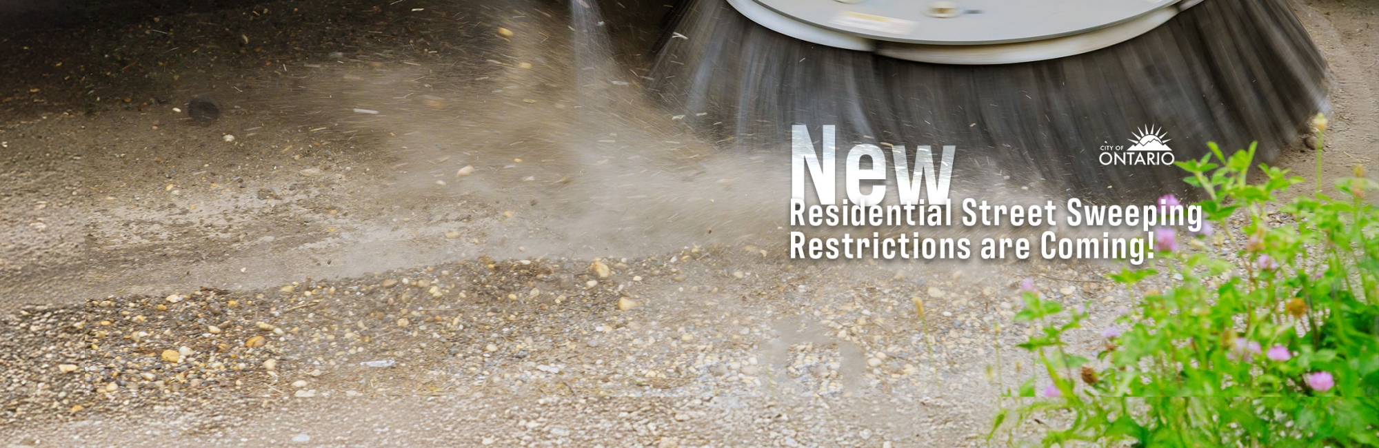 close up of bristles of a street sweeper on dirt, some greenery, text: "New Residential Street Sweeping Restrictions are Coming"