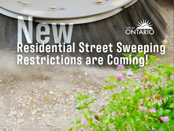 close up of bristles of a street sweeper on dirt, some greenery, text: "New Residential Street Sweeping Restrictions are Coming"